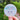 Round sticker with a snow girl face design held in front of a blurred natural background
