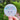 Round sticker with a snow girl face design held in front of a blurred natural background